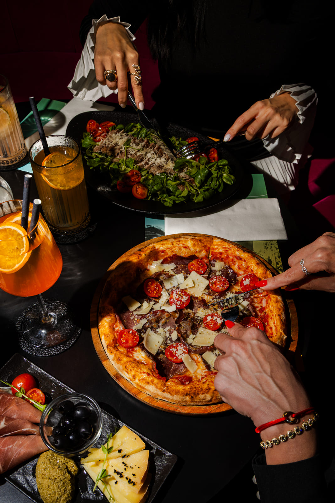 Woman slicing pizza next to salad and cocktails