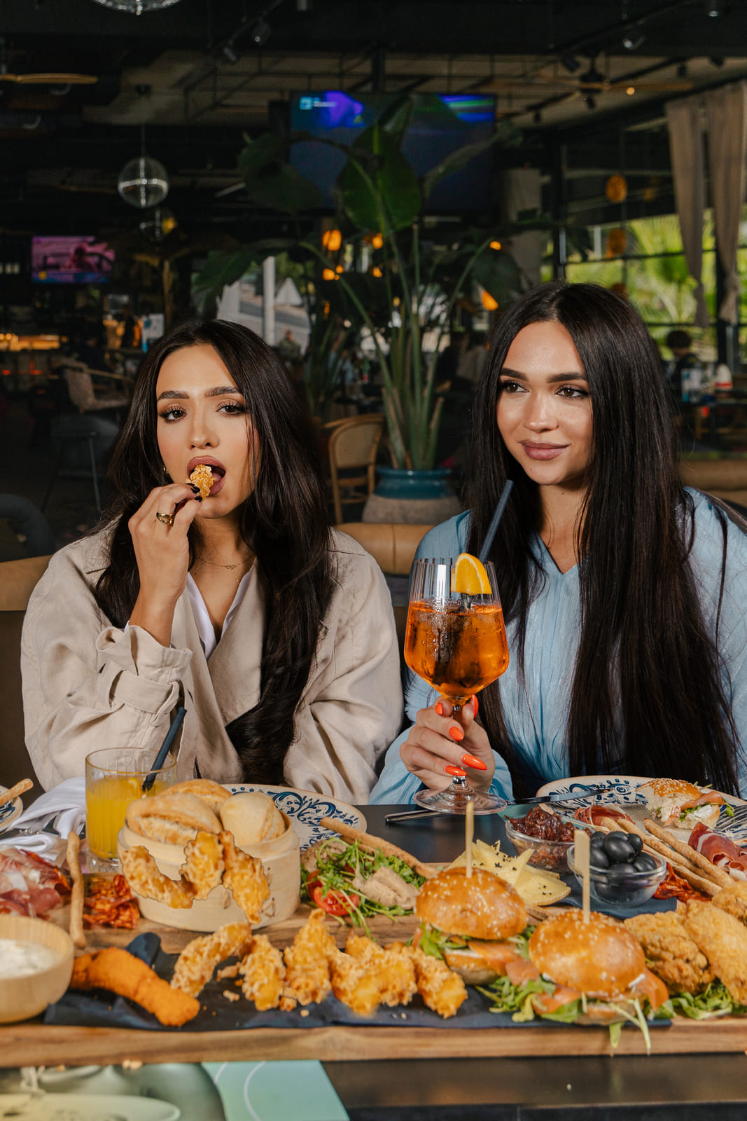 Two women sharing fried appetizers and cocktails at a colorful table