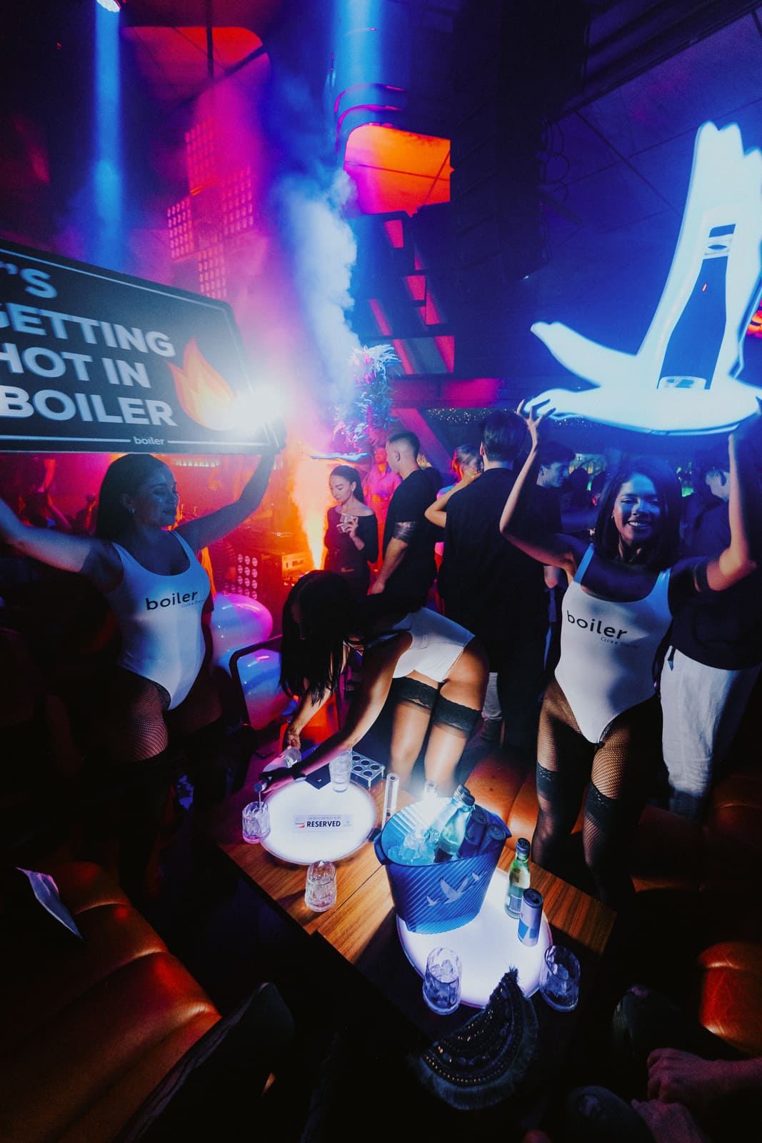 Bottle service team with signs and props serving a VIP table in a smoky nightclub with neon lights.