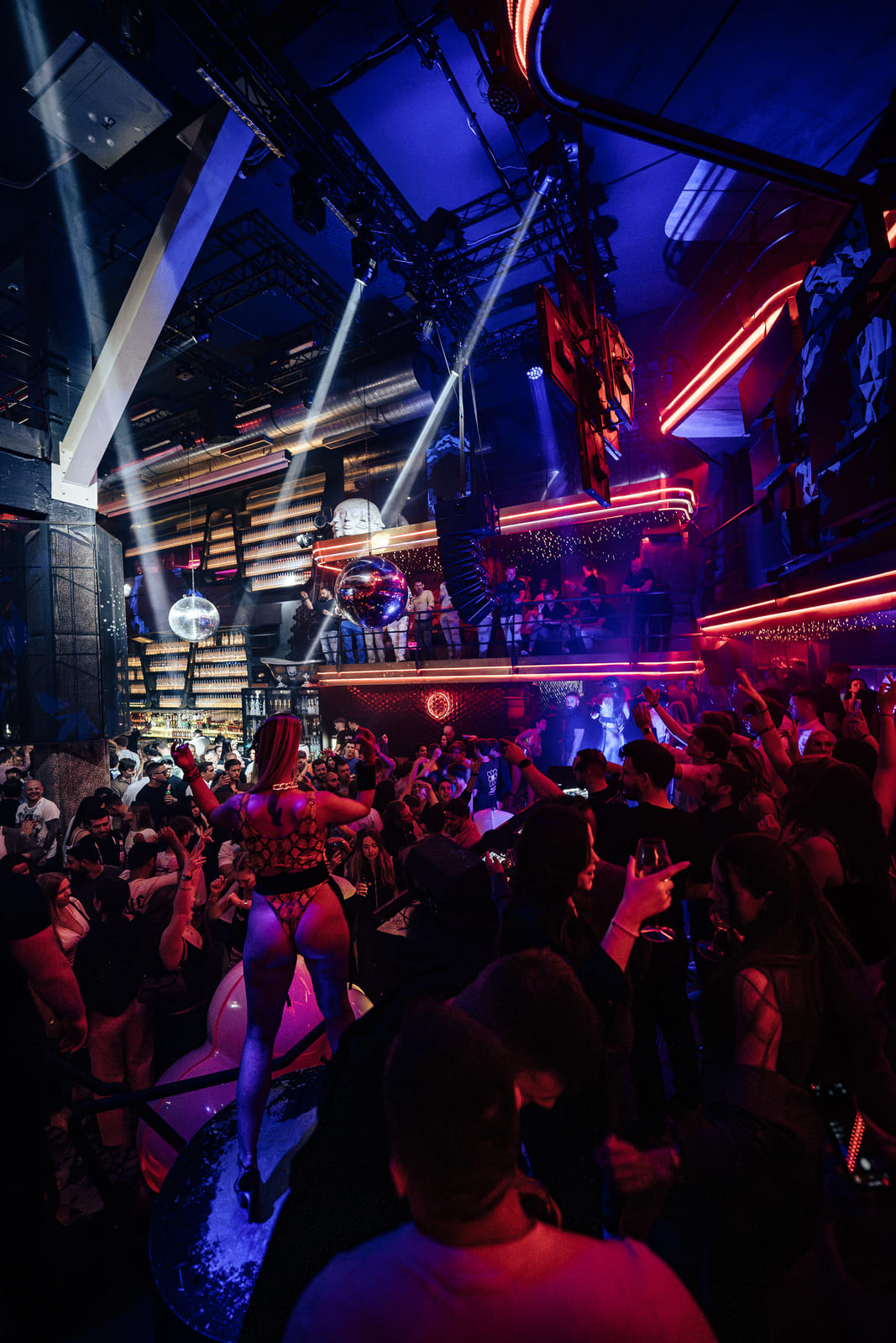 Dancer in red outfit performs on stage in a vibrant, packed nightclub.