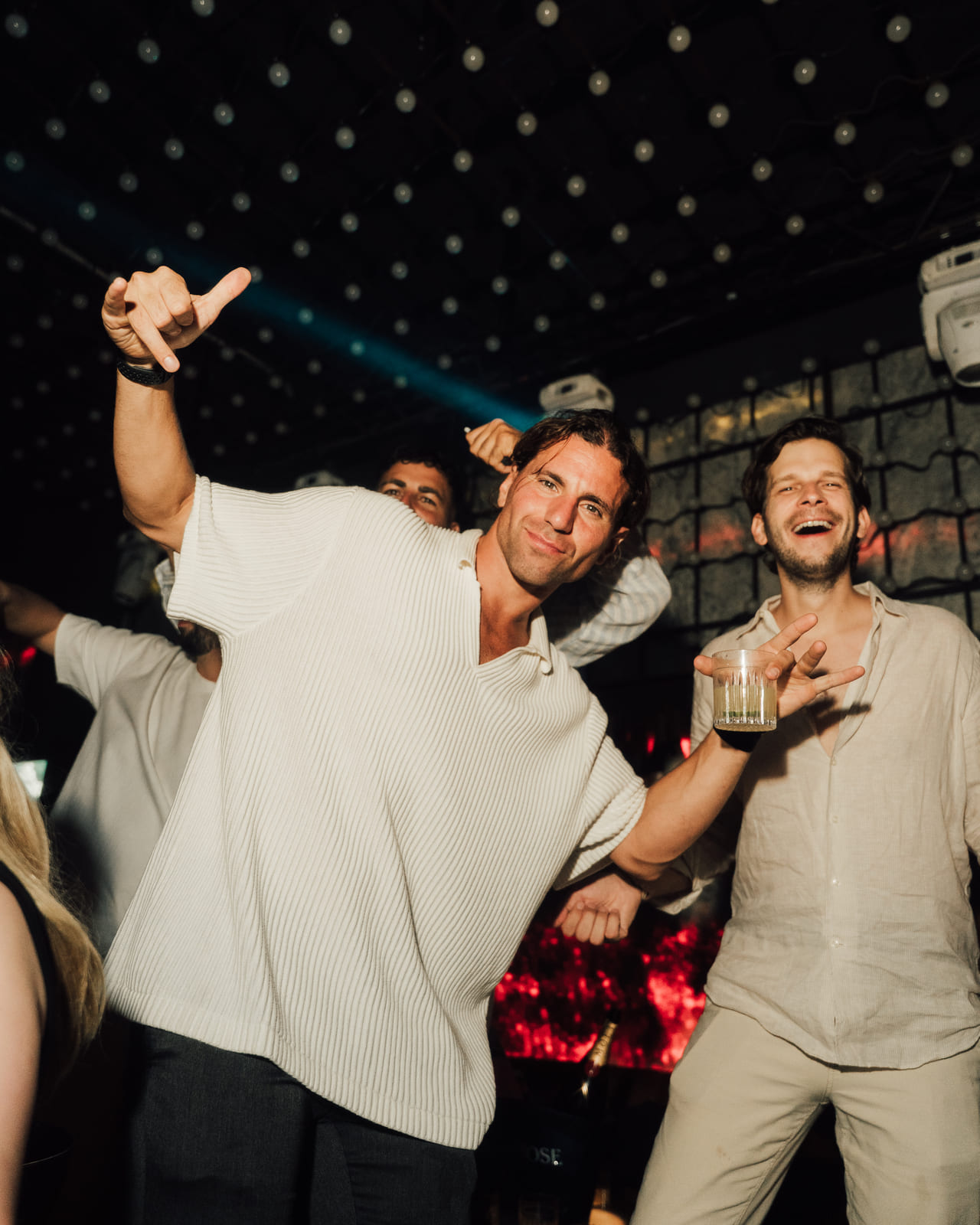 Group of men smiling and dancing in a club with dramatic lighting overhead