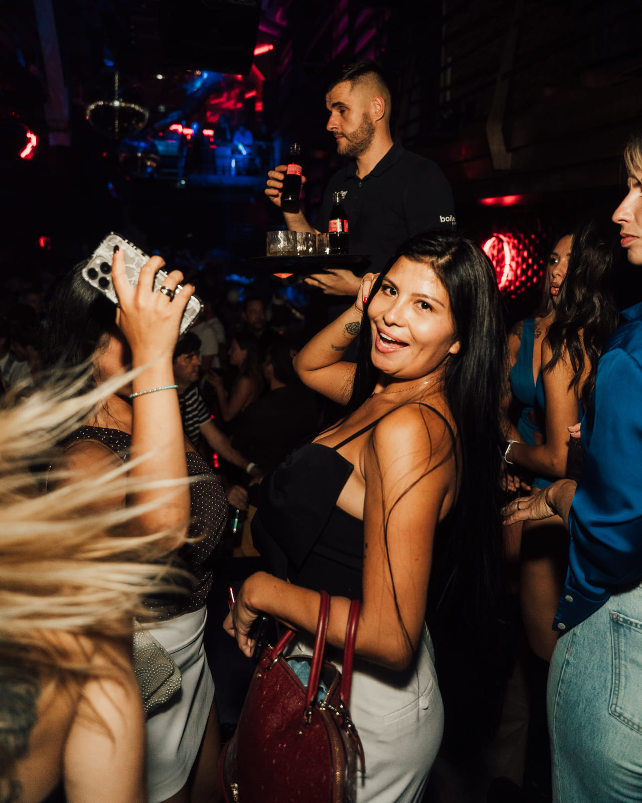 Woman smiling at the camera in a crowded nightclub with a server behind her