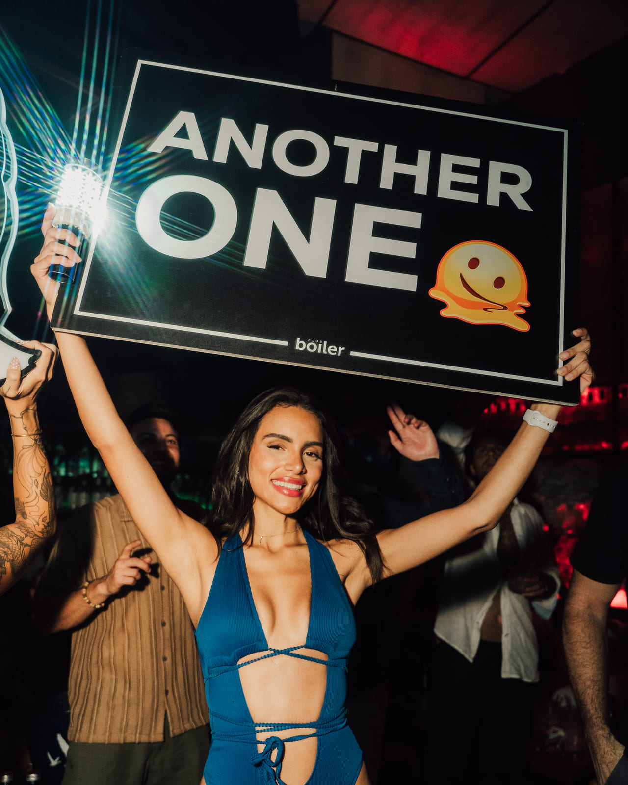Woman in blue outfit holding a sign that says “Another One” at a club