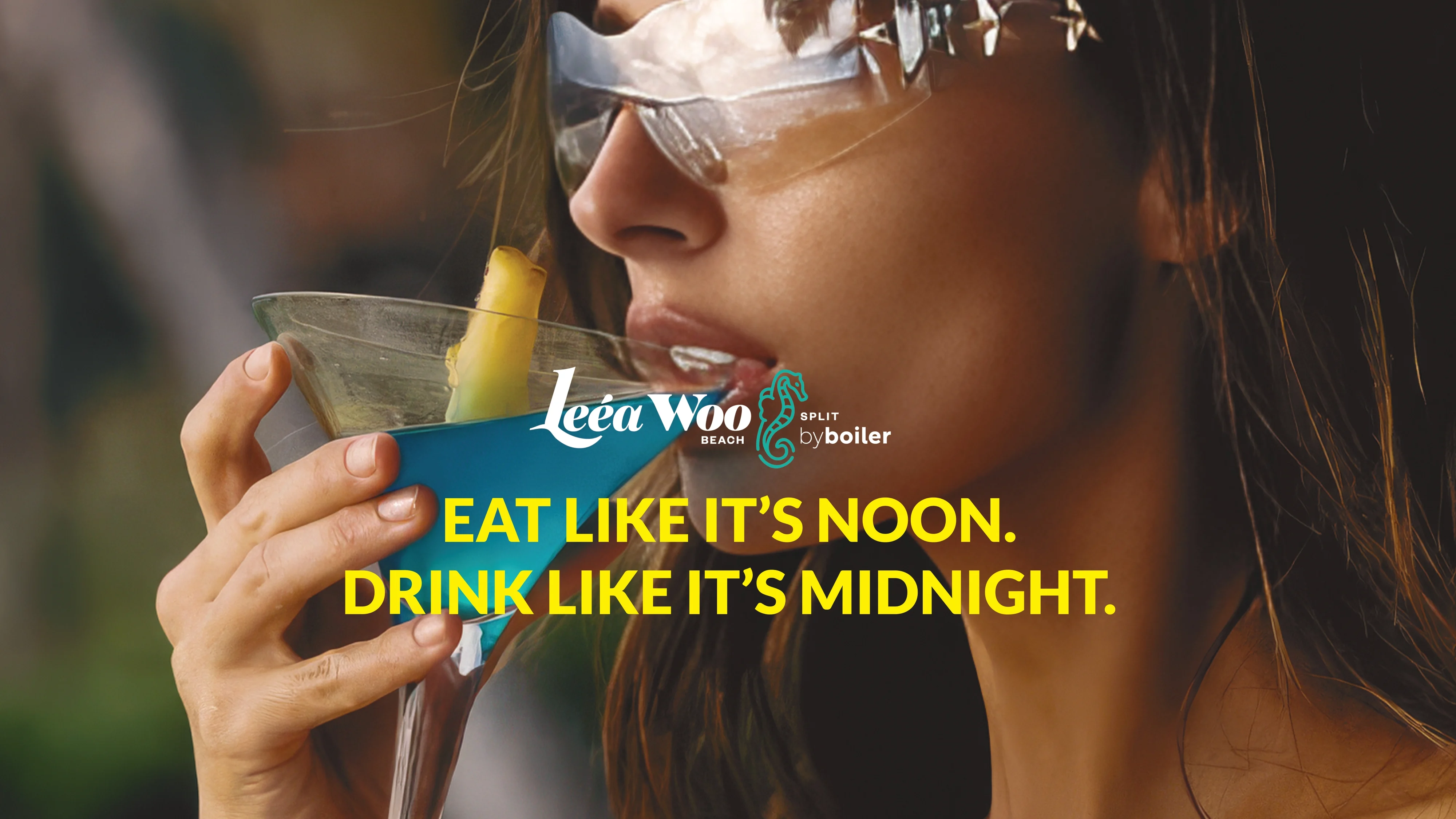 Woman wearing reflective sunglasses sipping a blue cocktail with a pineapple garnish at Leéa Woo Beach.
