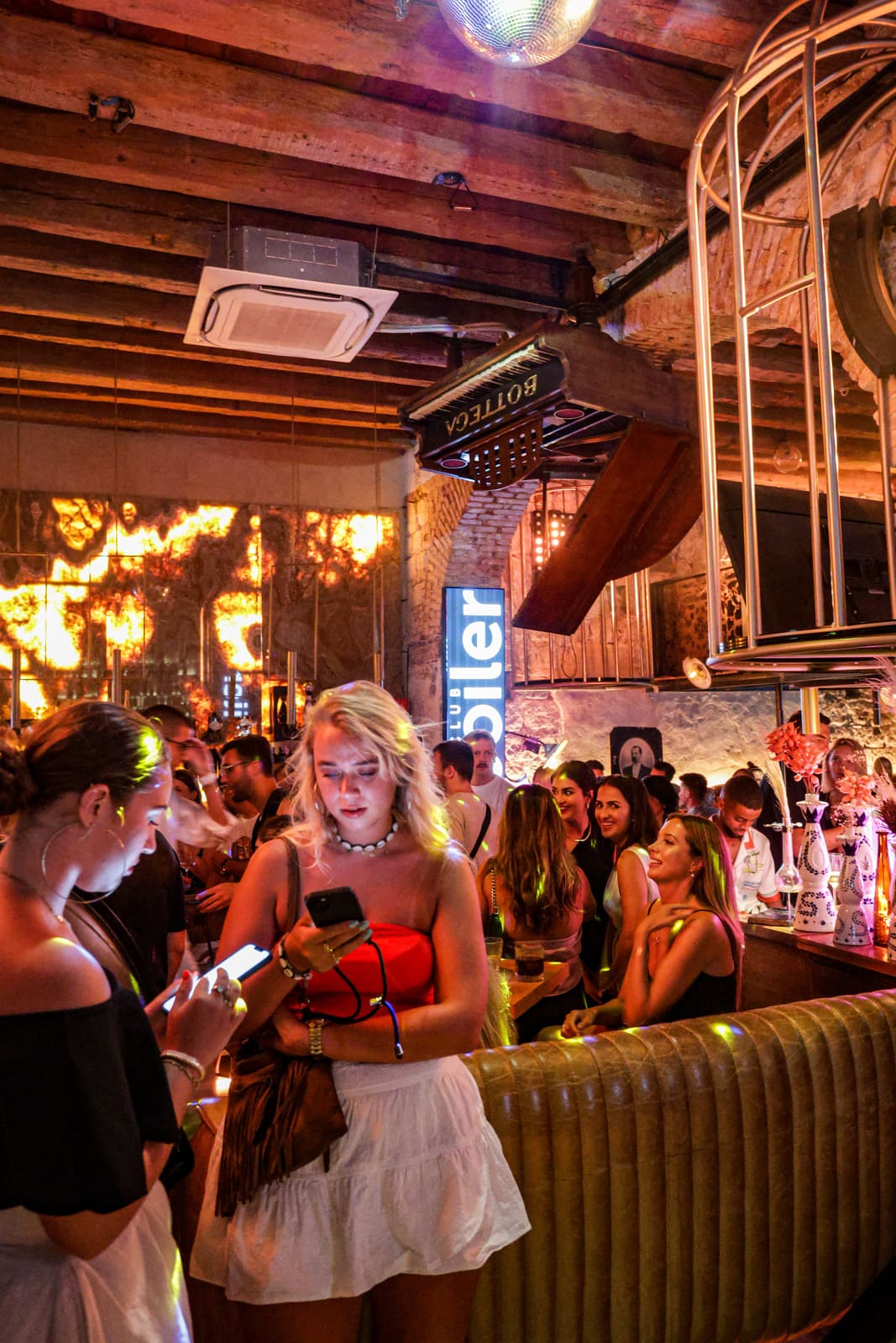Crowd of people gathered at a vibrant nightclub with neon signs and rustic decor.