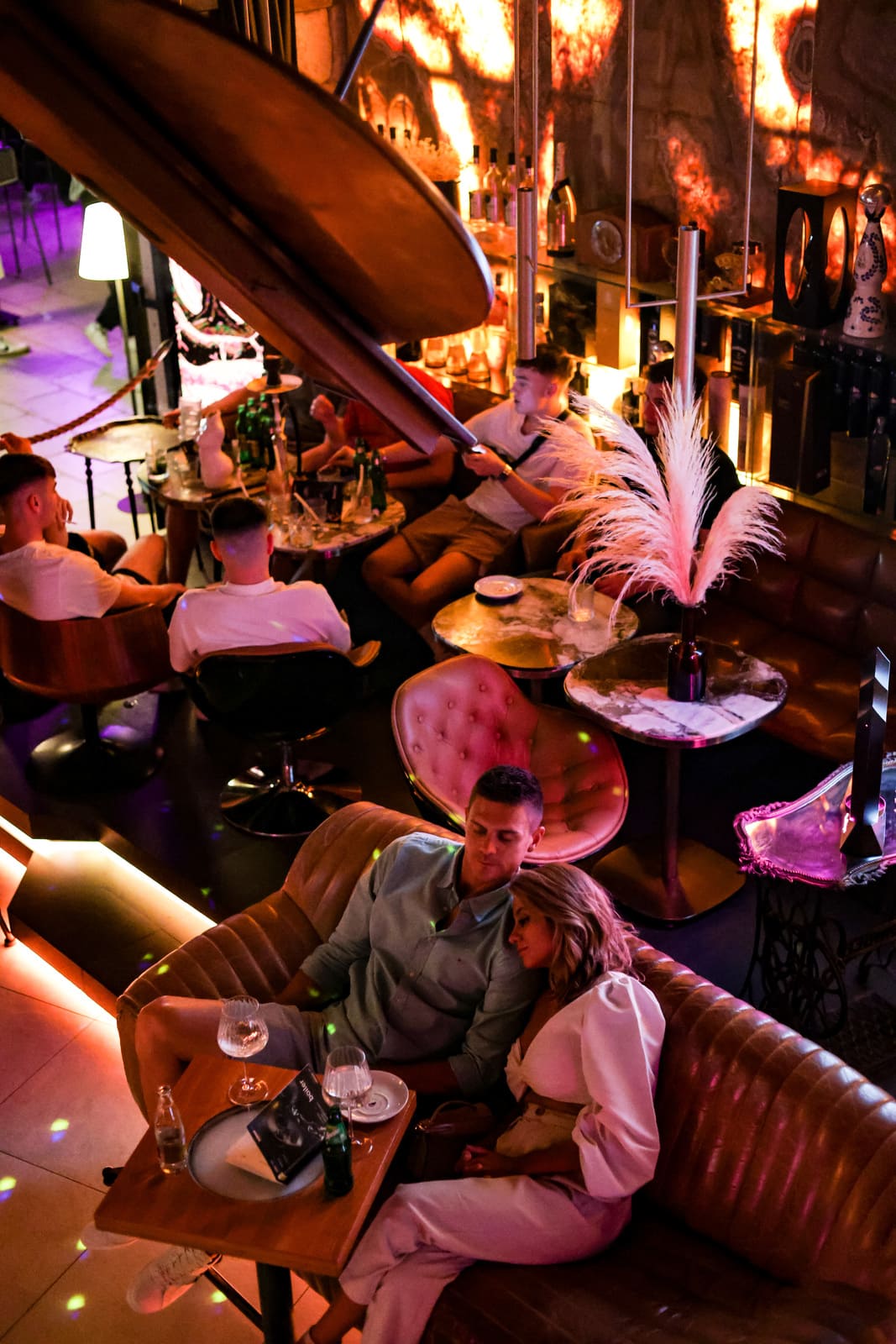 Couple relaxing on a leather couch in a dimly lit lounge with a piano overhead.