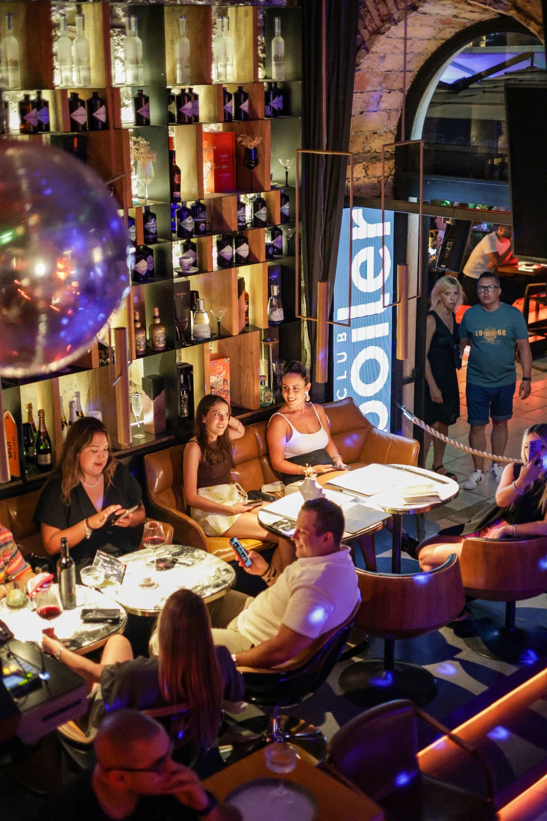 Groups socializing in a stylish lounge with bottle-lined walls at Boiler Club.