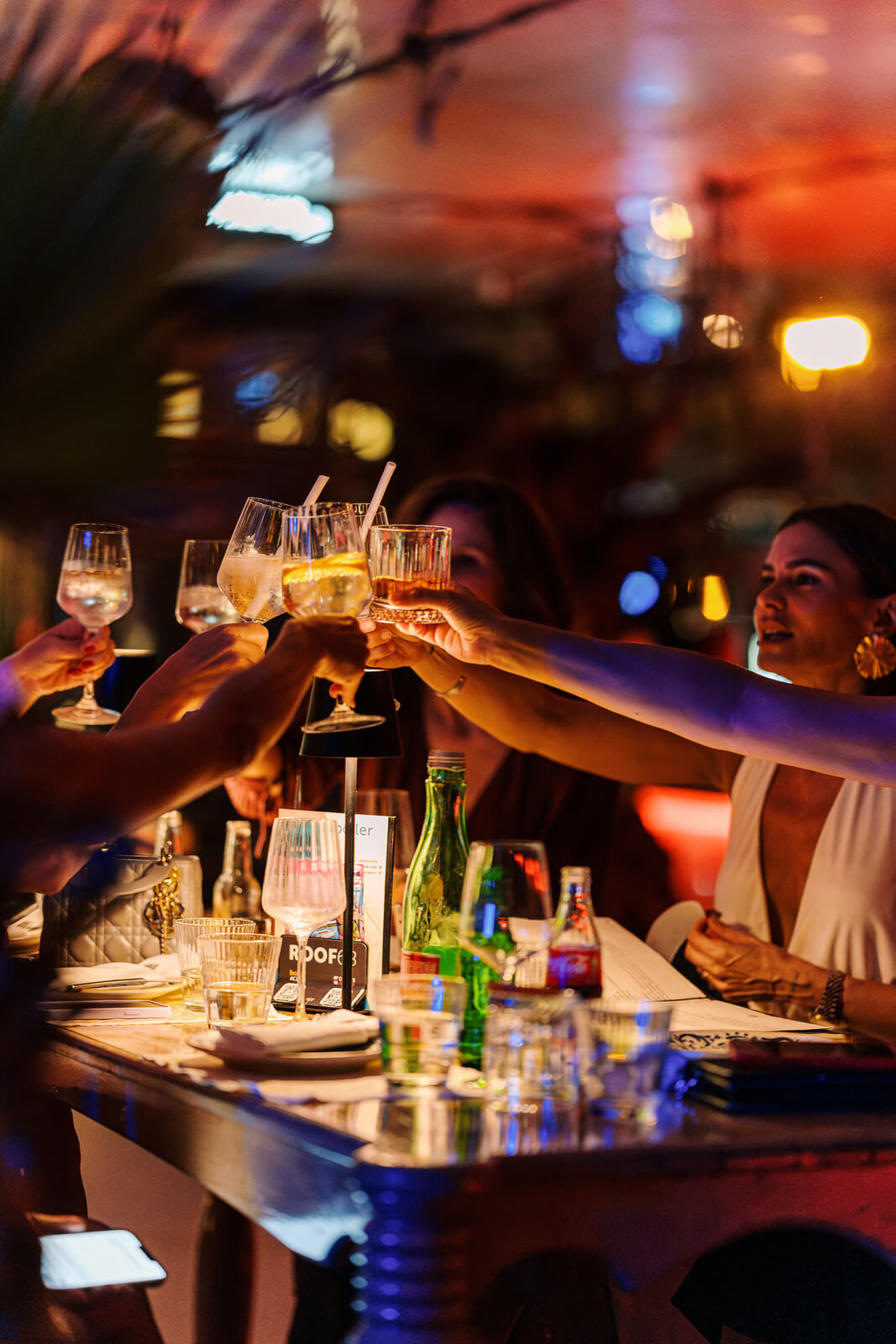 Group raising glasses in a toast at a dimly lit rooftop bar during evening celebration.