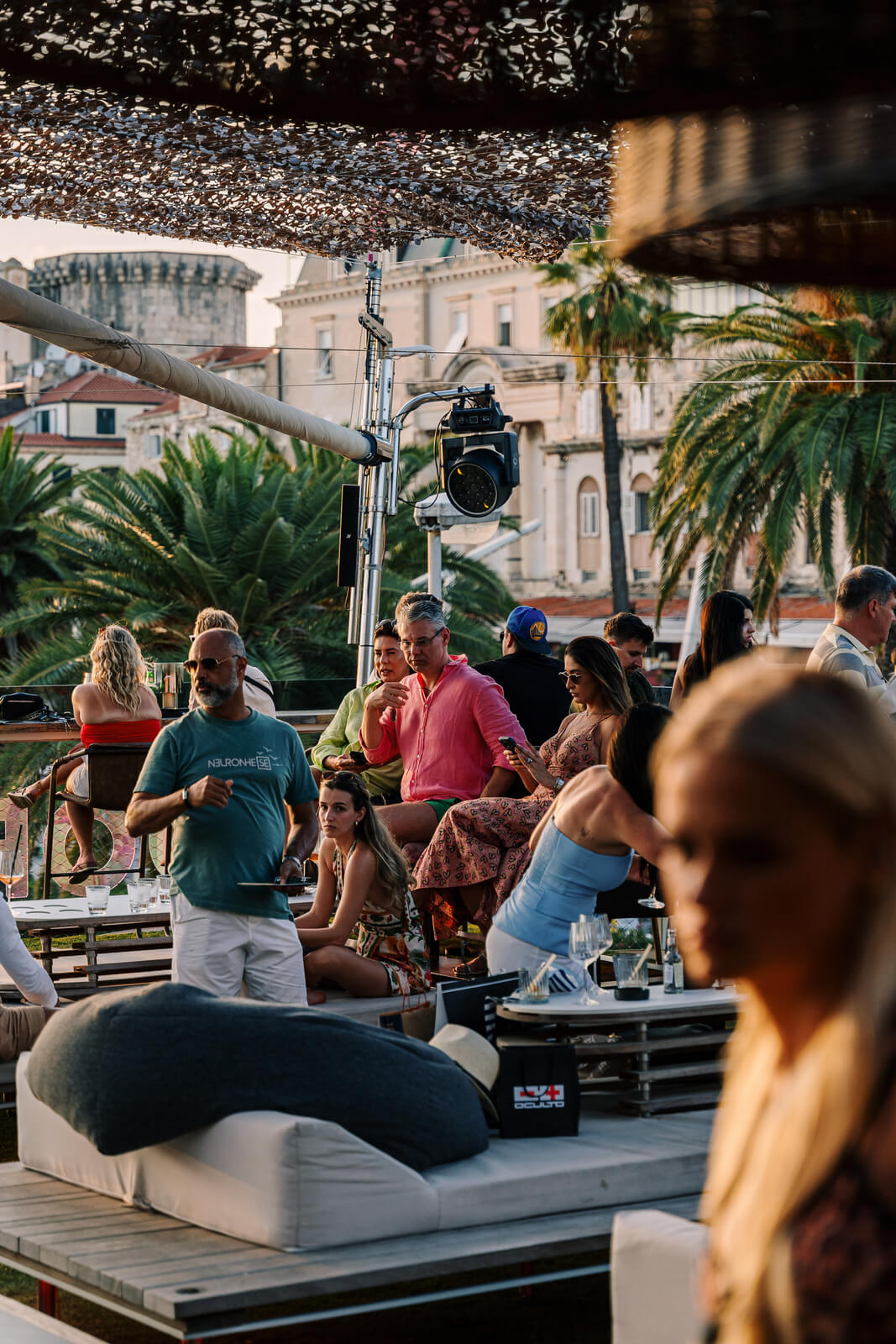 Guests relaxing on a rooftop lounge surrounded by palm trees and city views at golden hour.
