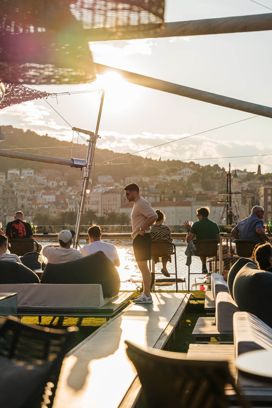 Guests relaxing on outdoor sofas watching sunset over the marina from a scenic rooftop lounge.