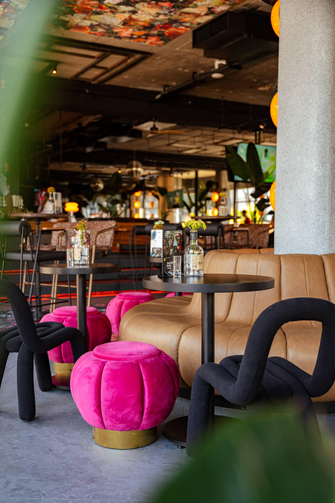 Modern lounge interior with tan leather seating, bright pink ottomans, and floral ceiling décor.