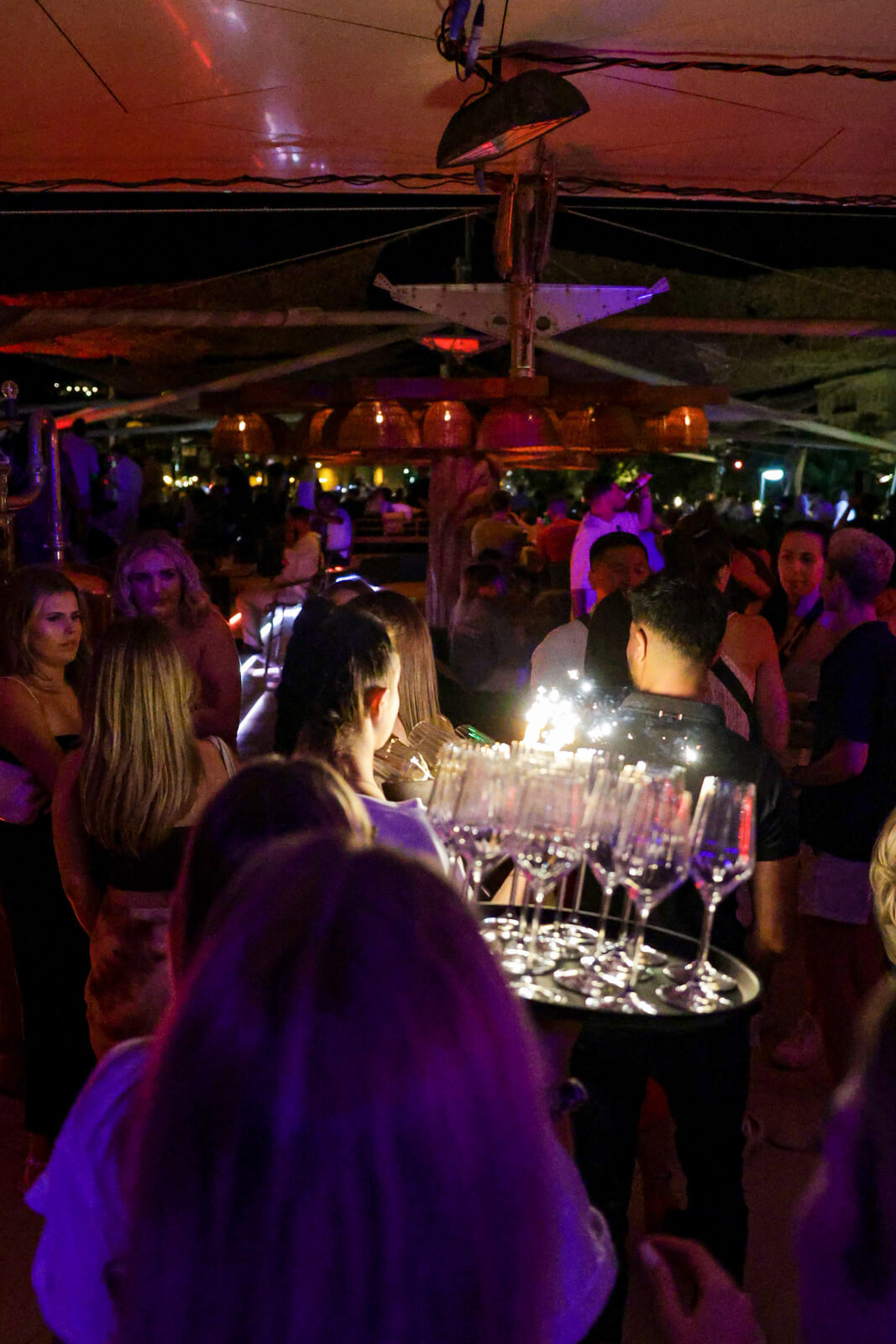 Nightclub crowd gathered under warm lights, with champagne glasses and sparklers being served.