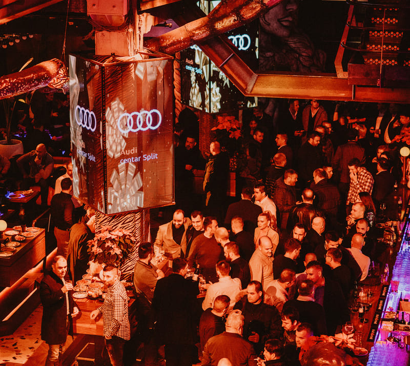 Large crowd gathered in a lively nightclub with Audi branding on digital screens and festive lighting.