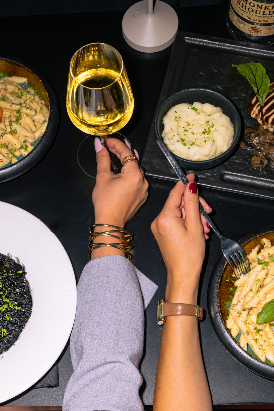 Overhead view of pasta dishes, mashed potatoes, and wine on a black table.