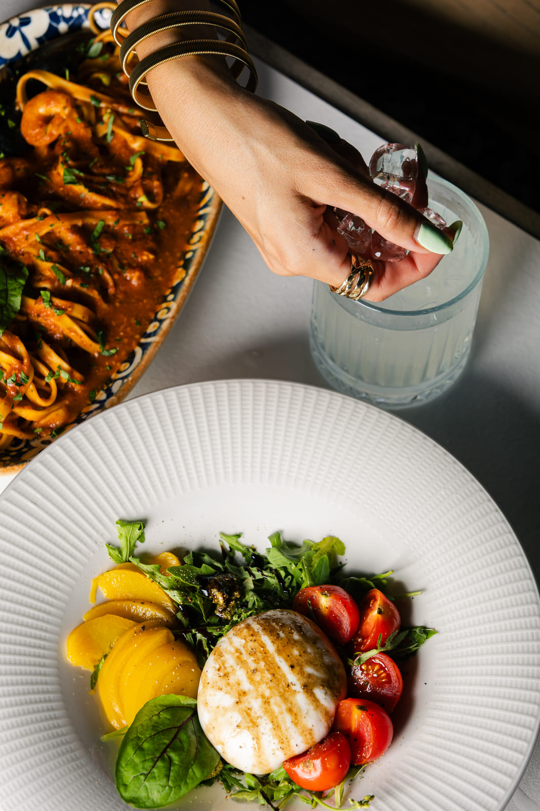 Burrata salad with peaches and tomatoes next to pasta in red sauce.