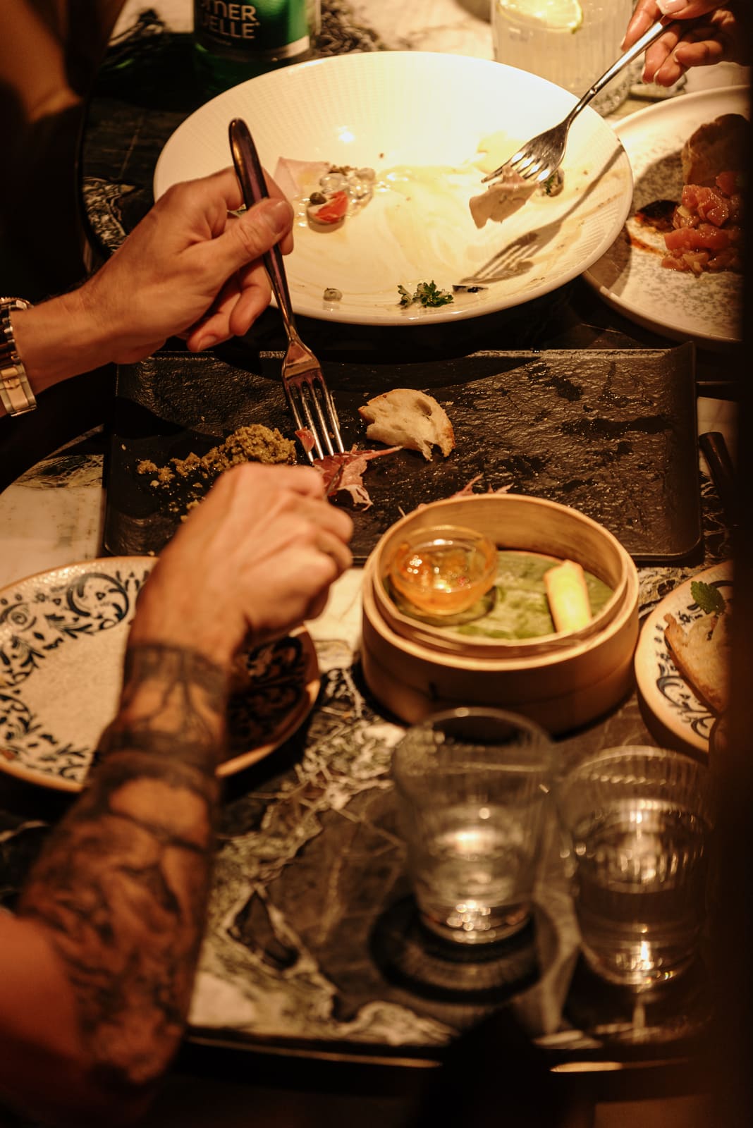 Diners sharing the last bites of a gourmet meal with rustic plates and dim lighting.